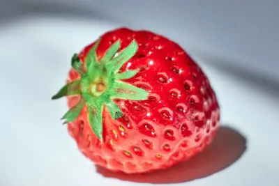 Eén verse rode aardbei met groen kroontje op een lichte ondergrond