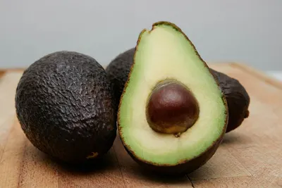 Twee hele avocado's en een doorgesneden avocado met pit op een houten plank