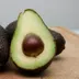 Twee hele avocado's en een doorgesneden avocado met pit op een houten plank