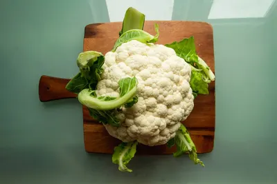 Een hele bloemkool met groene bladeren op een houten snijplank