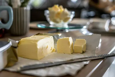 Blokjes boter en een pakje boter op bakpapier naast een botervlootje