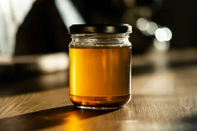 Een glazen pot met goudkleurige honing op een houten tafel