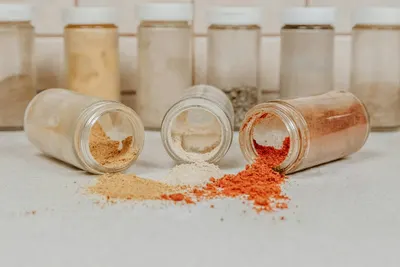 Glazen potjes met gedroogde kruiden en specerijen, waarvan een paar omgevallen