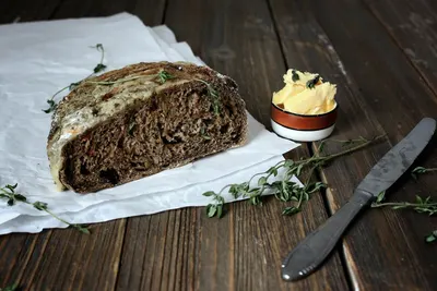 Een stuk donker brood met margarine en een mes op een houten tafel