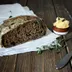 Een stuk donker brood met margarine en een mes op een houten tafel