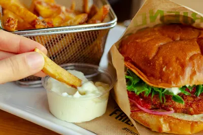 Een friet wordt in een bakje mayonaise gedoopt naast een hamburger