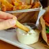 Een friet wordt in een bakje mayonaise gedoopt naast een hamburger
