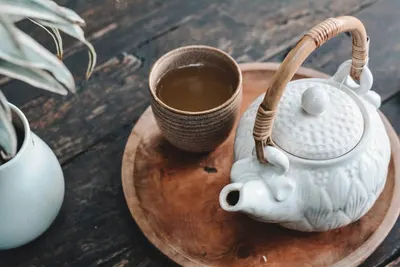 Een witte theepot en een kopje thee op een houten dienblad