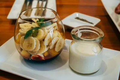 Een glas met yoghurt en banaan naast een potje yoghurt