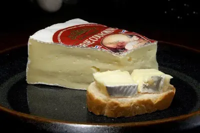 Een punt brie en een sneetje brood met brie op een donker bord