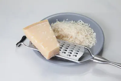 Een stuk Parmezaanse kaas met een rasp en geraspte kaas op een bord