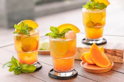Drie glazen oranje kombucha met sinaasappel en munt