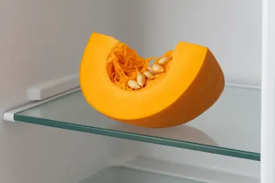 Een partje oranje pompoen met pitten op een koelkastplank