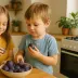 Twee kinderen pakken paarse pruimen uit een schaal in de keuken